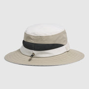 A beige and white bucket hat with a black mesh band and a small silver zipper pull, shown against a light gray background.