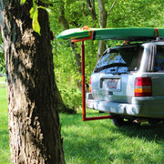 Silver SUV with a surfboard on top parked in a grassy area with trees.