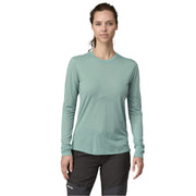 Woman wearing a light green long-sleeve shirt and black pants on a white background