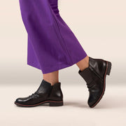 Black boots worn with purple pants on a beige background