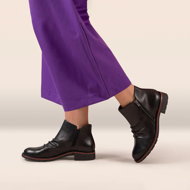 Black boots worn with purple pants on a beige background