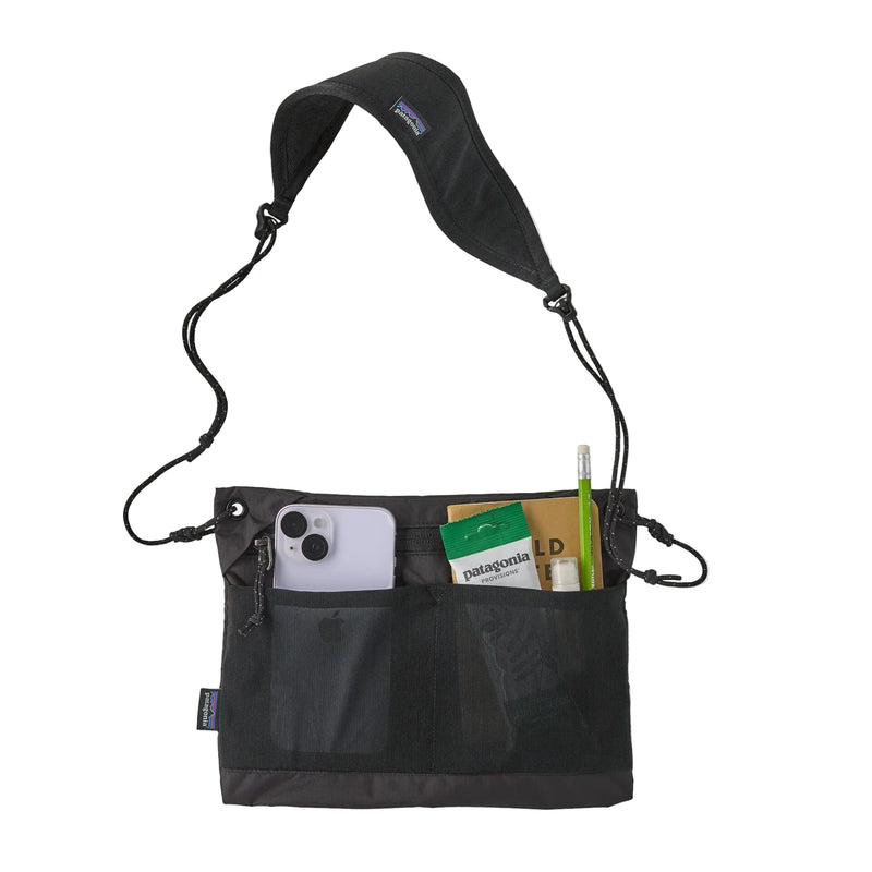 A black cross body bag holding gear on a white background