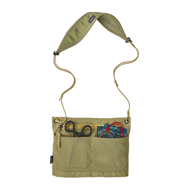 A green cross body bag holding gear on a white background