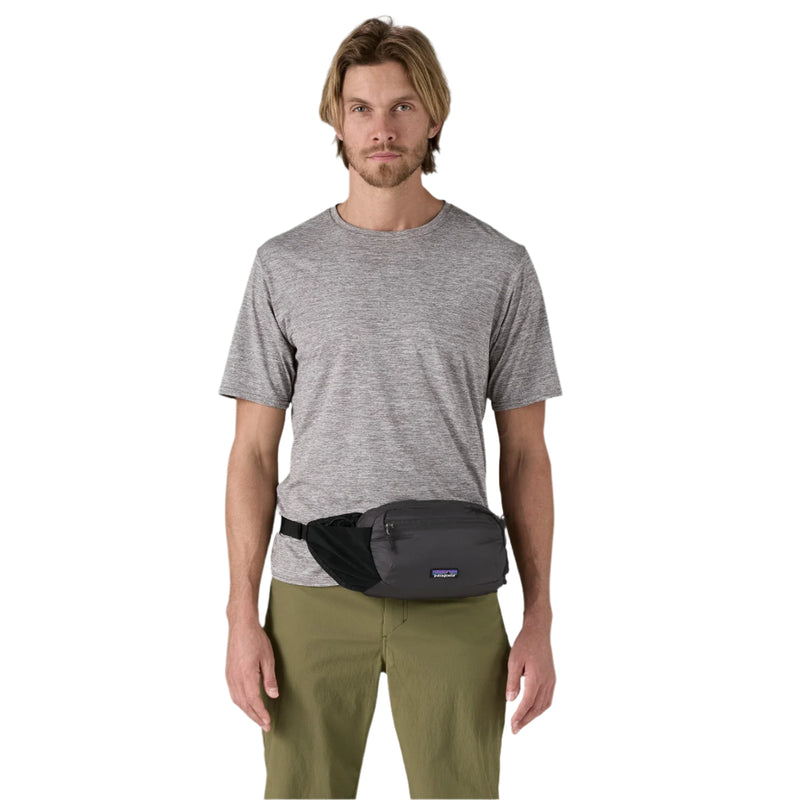 Man wearing a gray t-shirt and green pants with a black waist bag on a white background