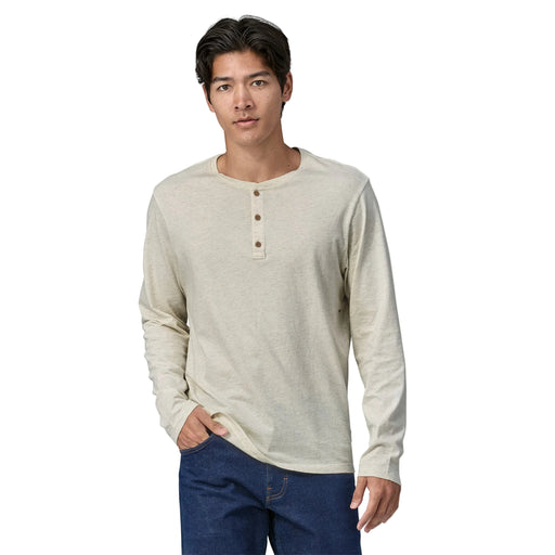 Man wearing a beige long-sleeve henley shirt and blue jeans on a white background