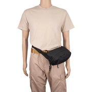 A black waist bag worn cross-body over a tan belt, displayed on a mannequin wearing a beige t-shirt and khaki cargo pants against a white background.