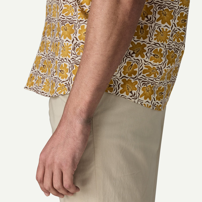Side view of a man wearing a white and yellow patterned shirt with grey shorts on a white background.