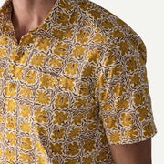 Close up of a man wearing a white and yellow patterned button down shirt on a white background.