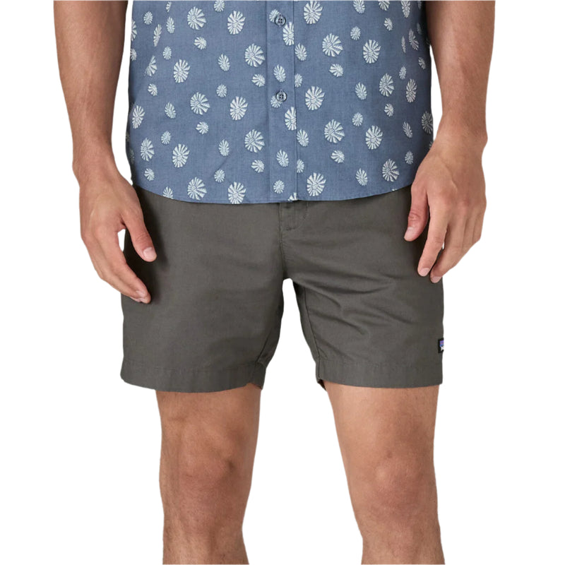 Person wearing a blue patterned shirt and gray shorts on a white background