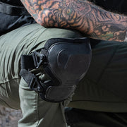 A person wearing black knee pads over pants squatting down