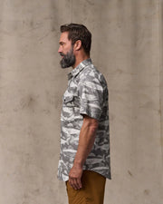 Man wearing a camouflage shirt against a beige wall