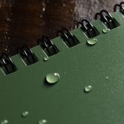 Green notebook with water droplets on a wooden surface