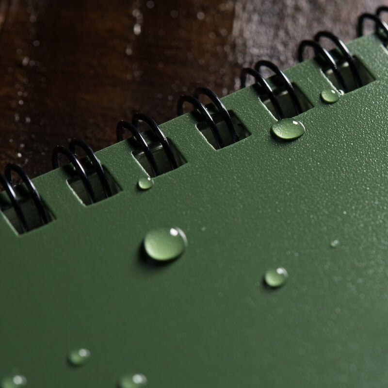 Green notebook with water droplets on a wooden surface