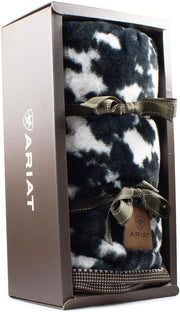Black and white cow print throw blanket wrapped in a ribbon and in a display box against a white background. 