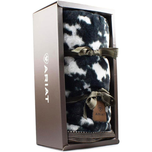Black and white cow print throw blanket wrapped in a ribbon and in a display box against a white background. 