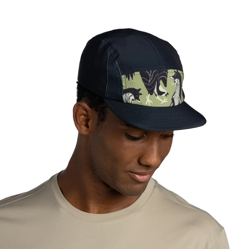 A man wearing a dark navy blue trucker-style cap with a green camouflage patterned front panel featuring black and white animal silhouettes, against a plain white background.