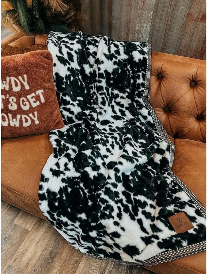 Black and white cow print throw blanket on a comfy brown couch. 