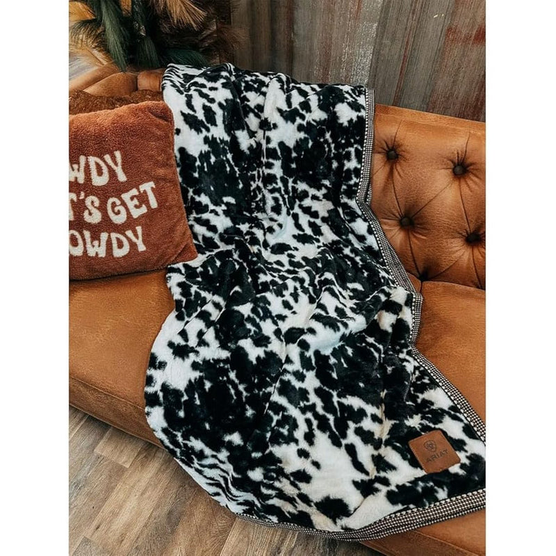 Black and white cow print throw blanket on a comfy brown couch. 