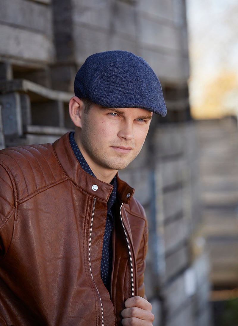 Man wearing a navy blue pub cap leaning up against a house. 