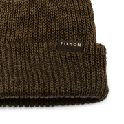 Close up of an olive colored beanie with a tan Filson logo against a white background. 