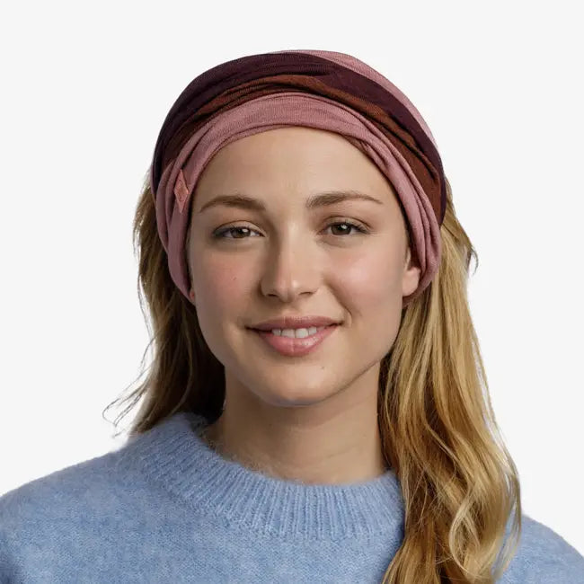 Woman wearing a pink and brown multifunctional neck gaiter as a headband against a white background