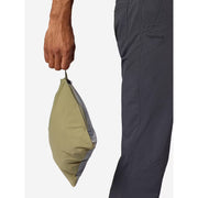 A close-up of a person holding a folded olive green Marmot pouch next to dark gray Marmot pants, against a light gray background.