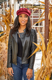 Woman wearing a red cabby cap standing next to some hay.
