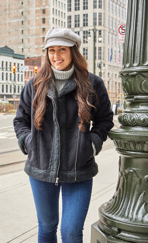 Woman wearing a light grey cabby cap walking down a city street. 