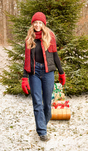 Woman wearing a red knit beanie pulling a festive sled in a forest. 