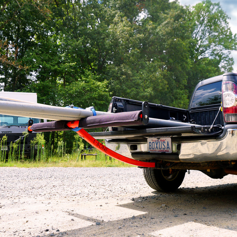 Red extender for boat attached to the back of a pickup truck with trees in the background.