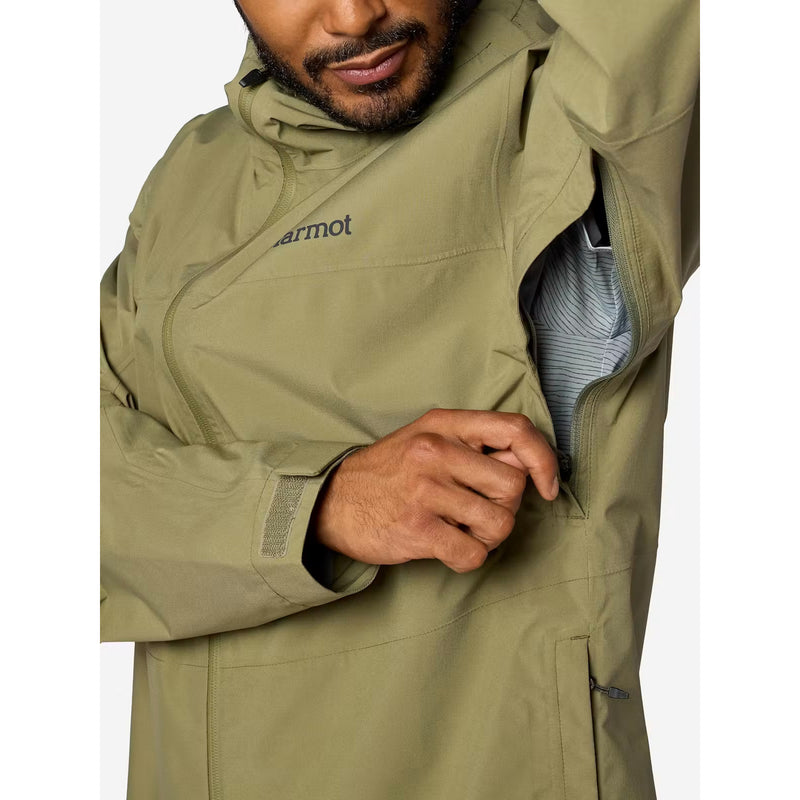 A close-up of a man wearing a Marmot olive green waterproof jacket, demonstrating a side zippered pocket that opens to reveal a striped shirt underneath.