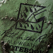 Close-up of a green notebook with a logo and text on a textured surface.