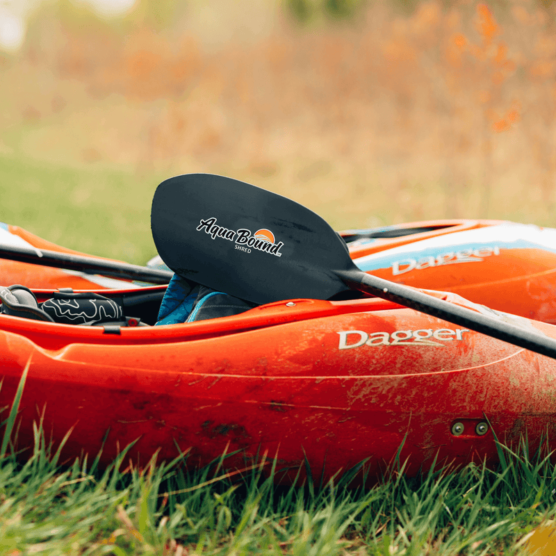 Red kayak with a black paddle on grass, featuring Aqua Bound and Dagger branding.