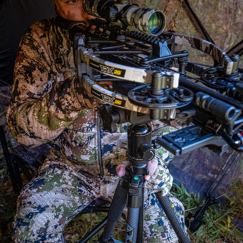 Person in camouflage attire using a crossbow on a tripod