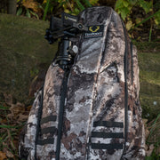 A TenPoint backpack in a brown and gray digital camouflage pattern, photographed outdoors against a mossy rock with fallen leaves. An Axis Tripod is visible in the pocket.