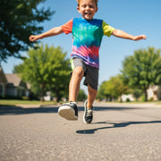 Child in a colorful tie-dye shirt running on a street with trees and houses in the background