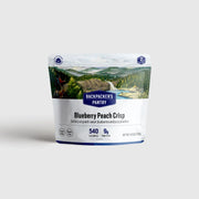 White and blue bag of freeze dried blueberry peach crisp with a picture of a mountain and a waterfall against a white background. 