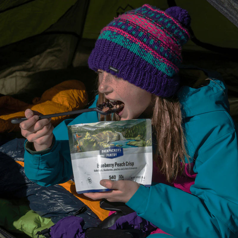 Girl with colorful hat eating a bag of blueberry peach crisp oatmeal.