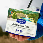 Backpacker's Pantry Blueberry Peach Crisp package held by a person with a scenic background