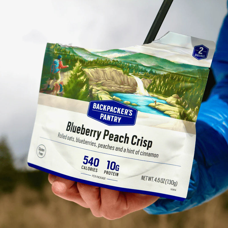 Backpacker's Pantry Blueberry Peach Crisp package held by a person with a scenic background