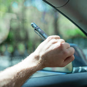 Hand using a car window breaking tool inside a vehicle with a blurred green outdoor background