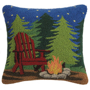 Decorative pillow with a red Adirondack chair, trees, and campfire design.