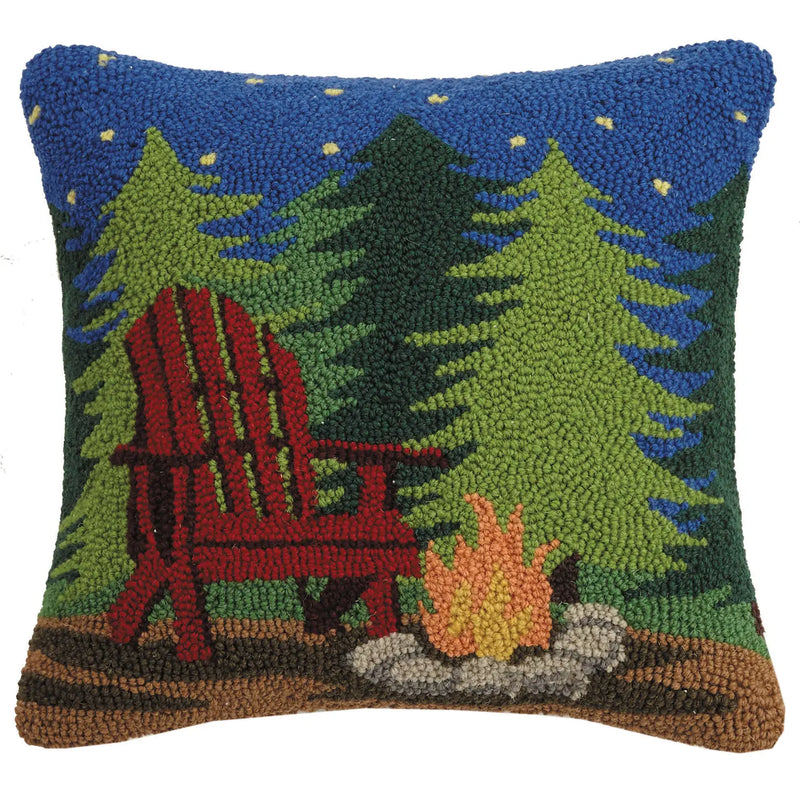 Decorative pillow with a red Adirondack chair, trees, and campfire design.