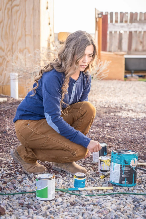 Woman wearing a pair of brown utility pants while opening cans of paint.