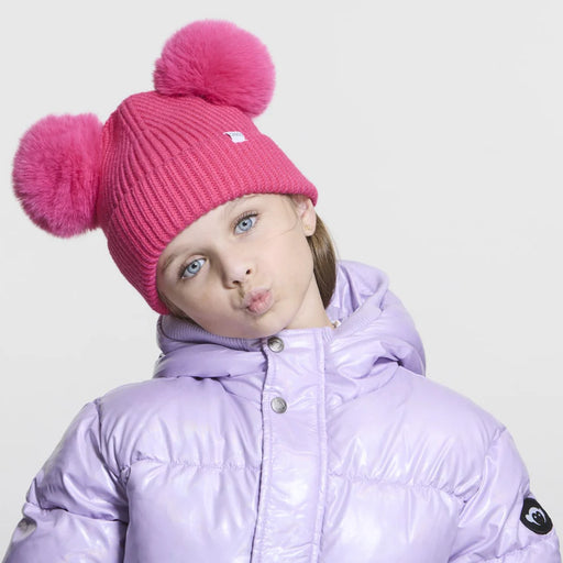 Girl wearing a pink pom pom beanie against a white background. 