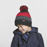 Boy wearing a black, grey, and red pom pom beanie against a white background. 