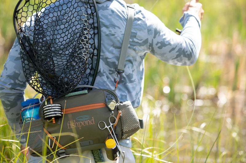 A person wearing a dark green bag filled with fishing gear walking through grass