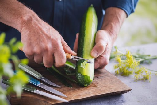 Man using a small peeler to peel a cucumber.