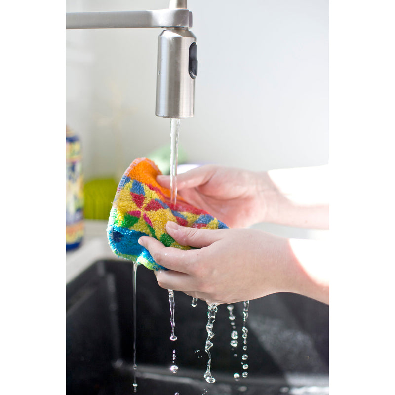 A close-up of a person's hands washing a bright, multicolored cleaning cloth under running water from a modern stainless steel faucet in a kitchen sink.