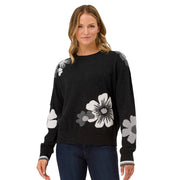 Woman wearing a black sweater with floral patterns on a plain background
